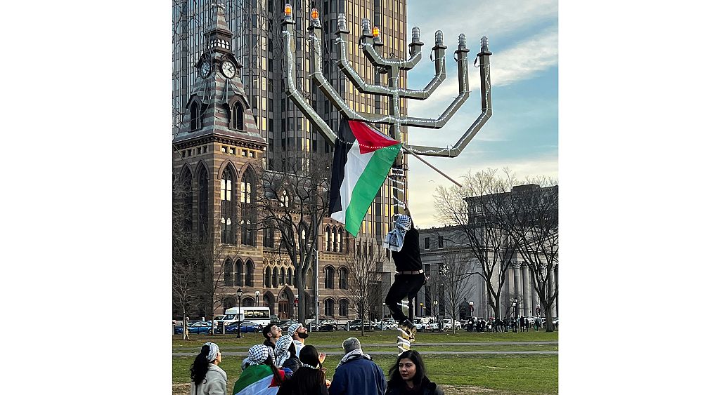 شاهد: متظاهر يعلّق علم فلسطين على شمعدان يهودي عملاق في الولايات المتحدة