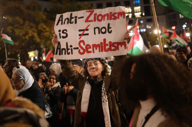 BERLIN, GERMANY - NOVEMBER 04: People, including a young woman holding a sign that reads:" Anti-Zionism is not anti-Semitism," chant slogans and carry Palestinian flags as they arrive at Potsdamer Platz during a "Freedom for Palestine" protest march that drew thousands of participants on November 04, 2023 in Berlin, Germany. Meanwhile in Gaza Israeli forces have encircled Gaza City as fighting with Hamas fighters continues to rage. (Photo by Sean Gallup/Getty Images)