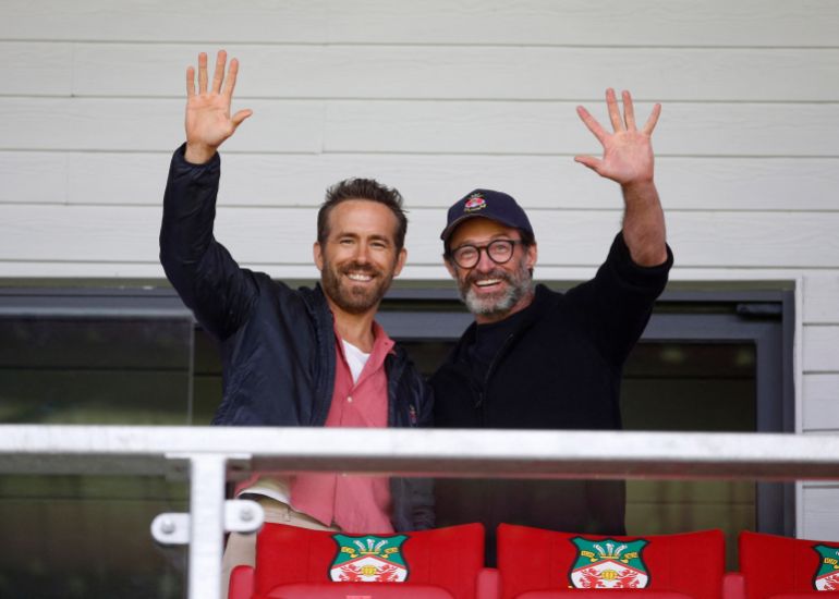 رايان رينولدز ، المالك المشارك في Wrexham ، وممثله هيو جاكمان يصورون صورة في المدرجات