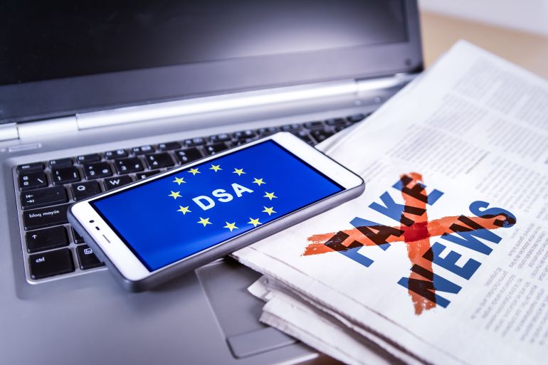 Smartphone with DSA and EU flag on screen over a newspaper with Fake news and a laptop. Fake news, HOAX concept