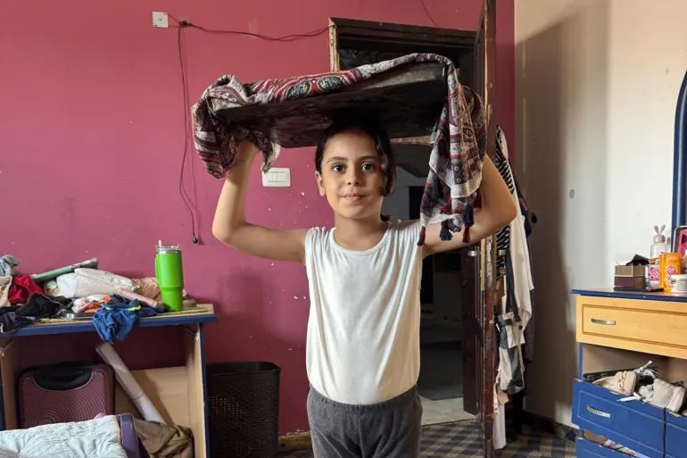 The author’s daughter, Banias, demonstrates how her father carries the bread to be baked at the public oven [Maram Humaid/Al Jazeera]